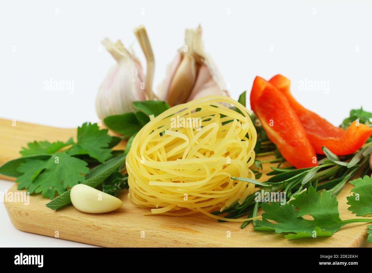 Closeup of uncooked tagliatelle, fresh herbs, garlic and red pepper on wooden surface Stock Photo