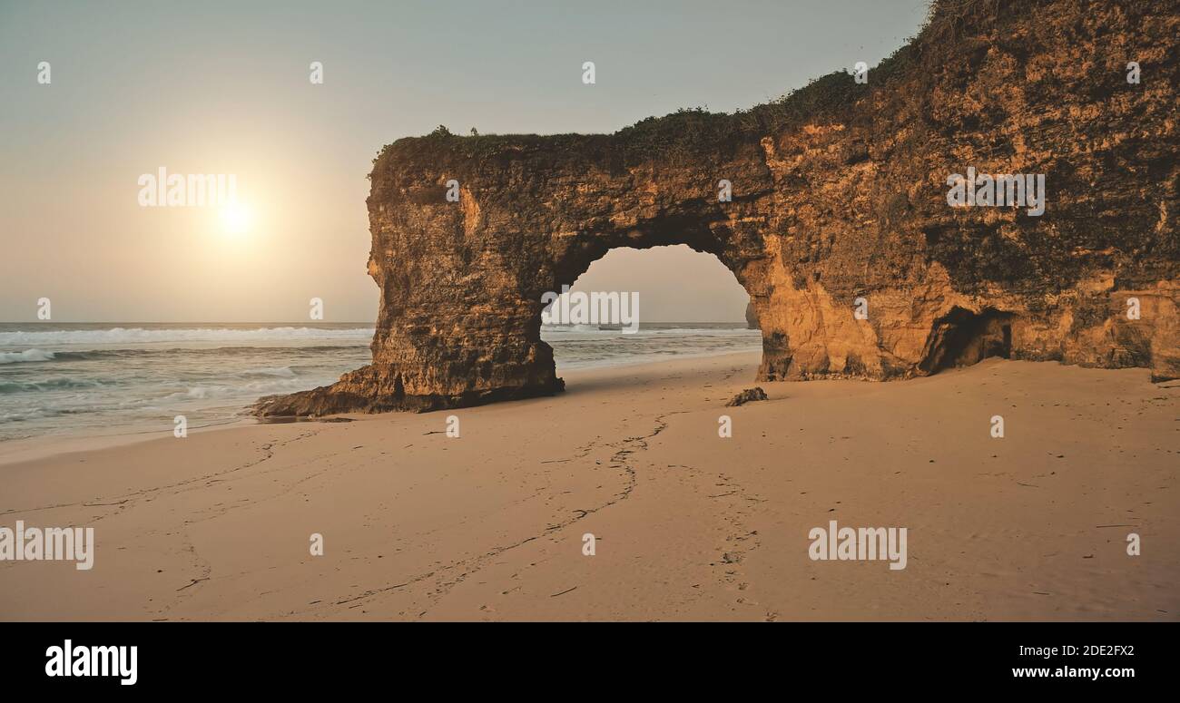 Aerial view of sun over rock wall with hole at sand beach sea shore. Unique geological formation at Bawana Beach, Sumba Island, Indonesia, Asia. Nobody nature landscape with ocean water waves Stock Photo
