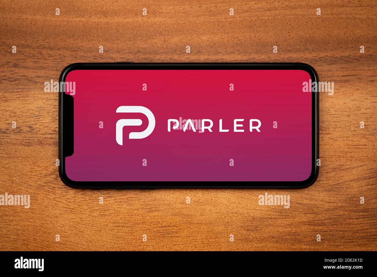 A smartphone showing the Parler logo rests on a plain wooden table (Editorial use only). Stock Photo