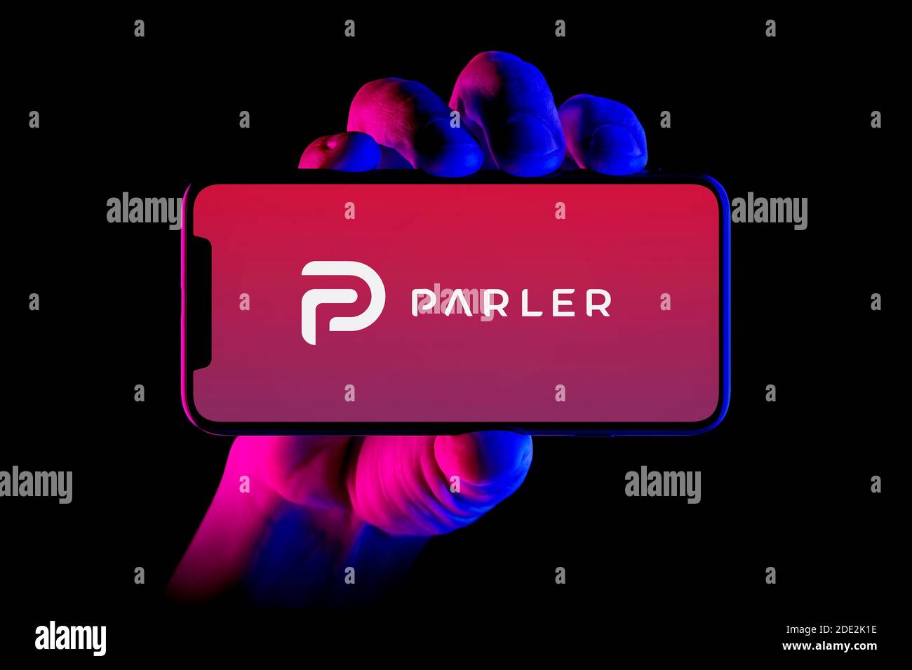 A smartphone displaying the Parler logo is held by a hand shot on a black background (editorial use only). Stock Photo