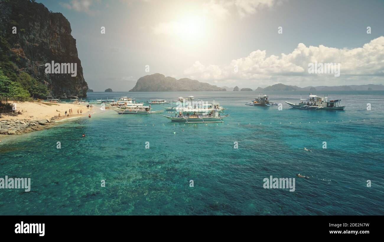 Aerial sun beach at ocean harbor with boats on azure water. Travelers relaxing on tropical resort at sand coast. Greenery mount with forest trees at summer sunny day. Cinematic drone shot Stock Photo