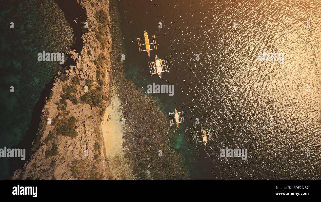 Top down sunset of ocean harbour with passenger boats aerial view. Tropical island with rock shore and sand beach at sun set light. Dark seascape at summer cruise scenery in drone shot Stock Photo