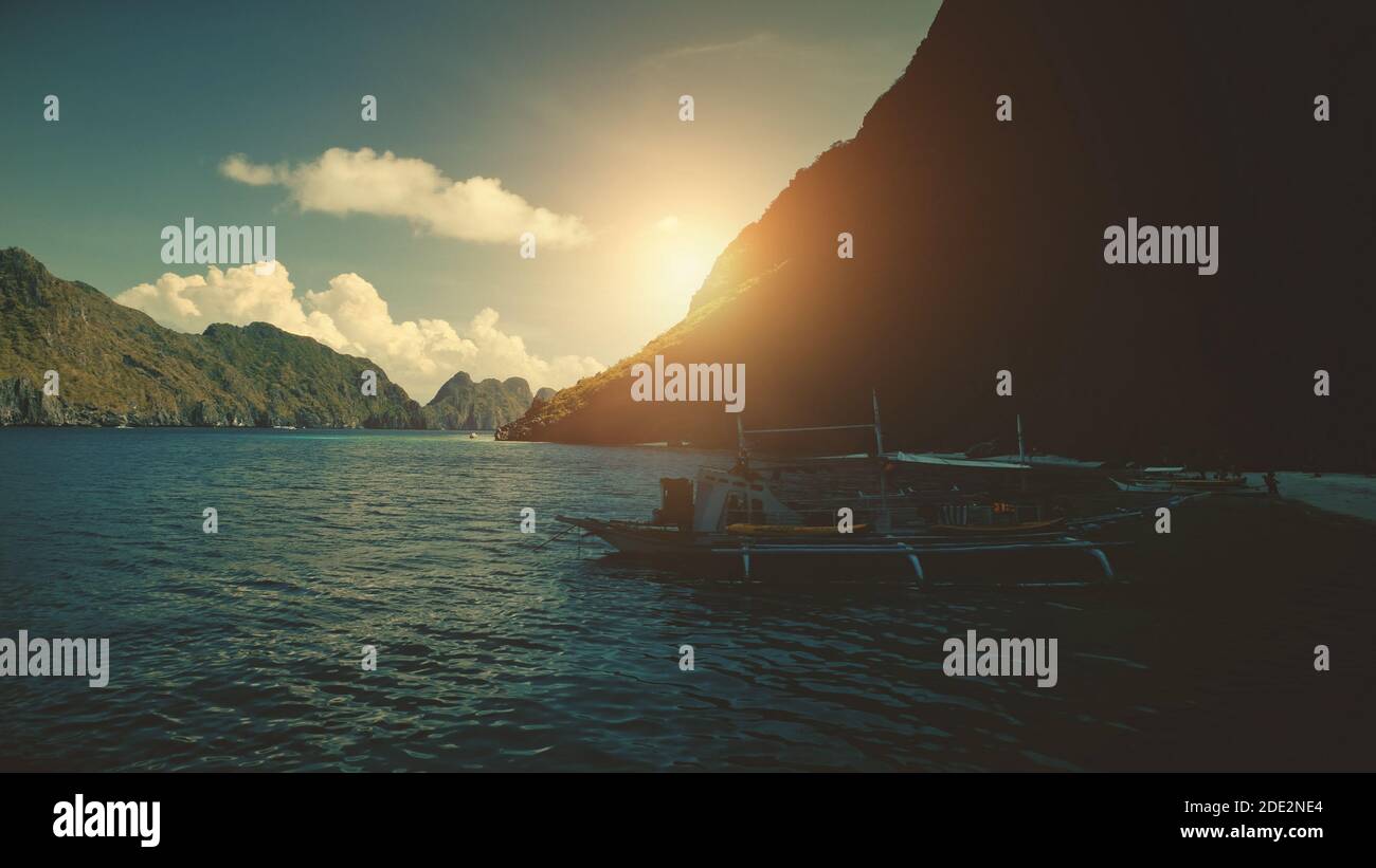 Closeup of traditional passenger boat at sand ocean coast in aerial view. Mountain island silhouette at sun light. People rest at sandy beach. Majestic summer cruise tour at El Nido isles, Philippine Stock Photo