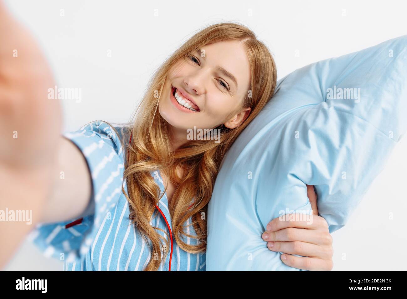 Excited beautiful young woman in pajamas holds a soft pillow and smiles ...