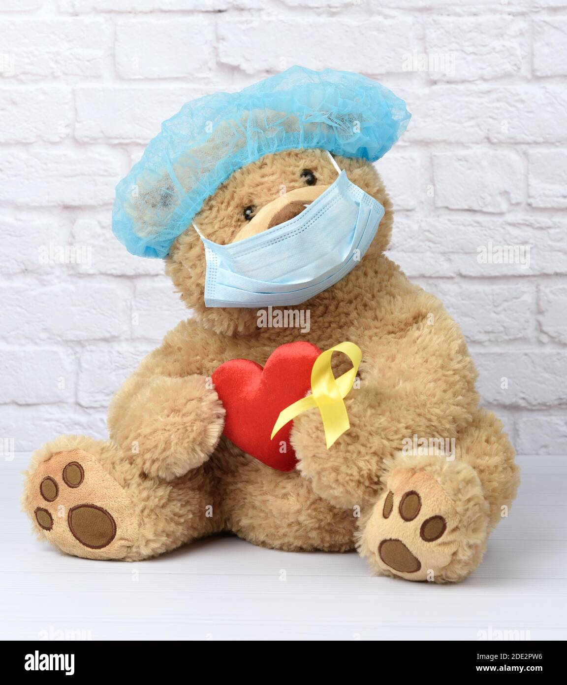 brown teddy bear holds in his paw a yellow ribbon folded in a loop, concept of the fight against childhood cancer. problem of suicides and their preve Stock Photo