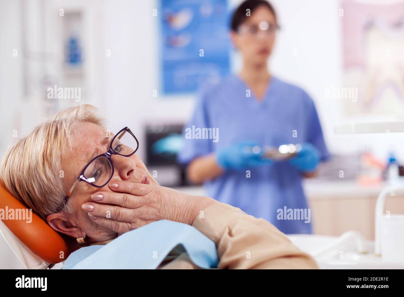 Elderly patient in pain at dentist clinic waiting diagnosis from doctor in medical office. Senior woman in healthcare hospital accusing and complaining about tooth. Stock Photo