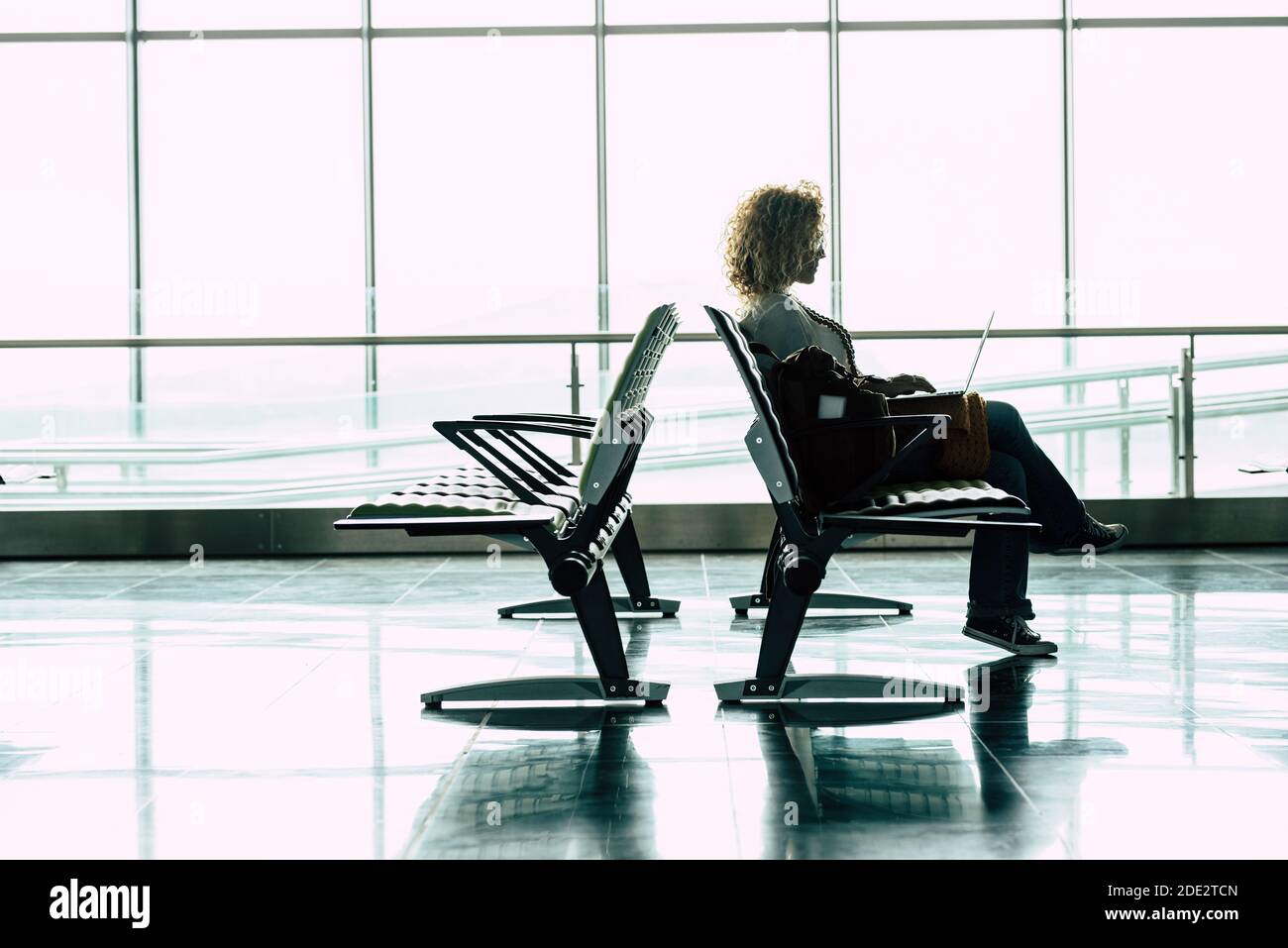 Travel and work online job people at the airport gate - woman sit down and wait for her flight with laptop computer in smart working or digital nomad Stock Photo