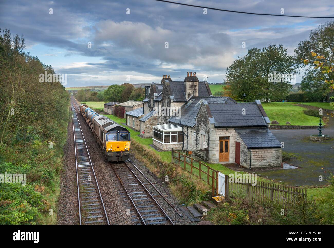 Direct Rail Services class 66 locomotive hauling  Network Rail Railhead treatment train dealing with autumn leaves passing the closed Arkholme station Stock Photo