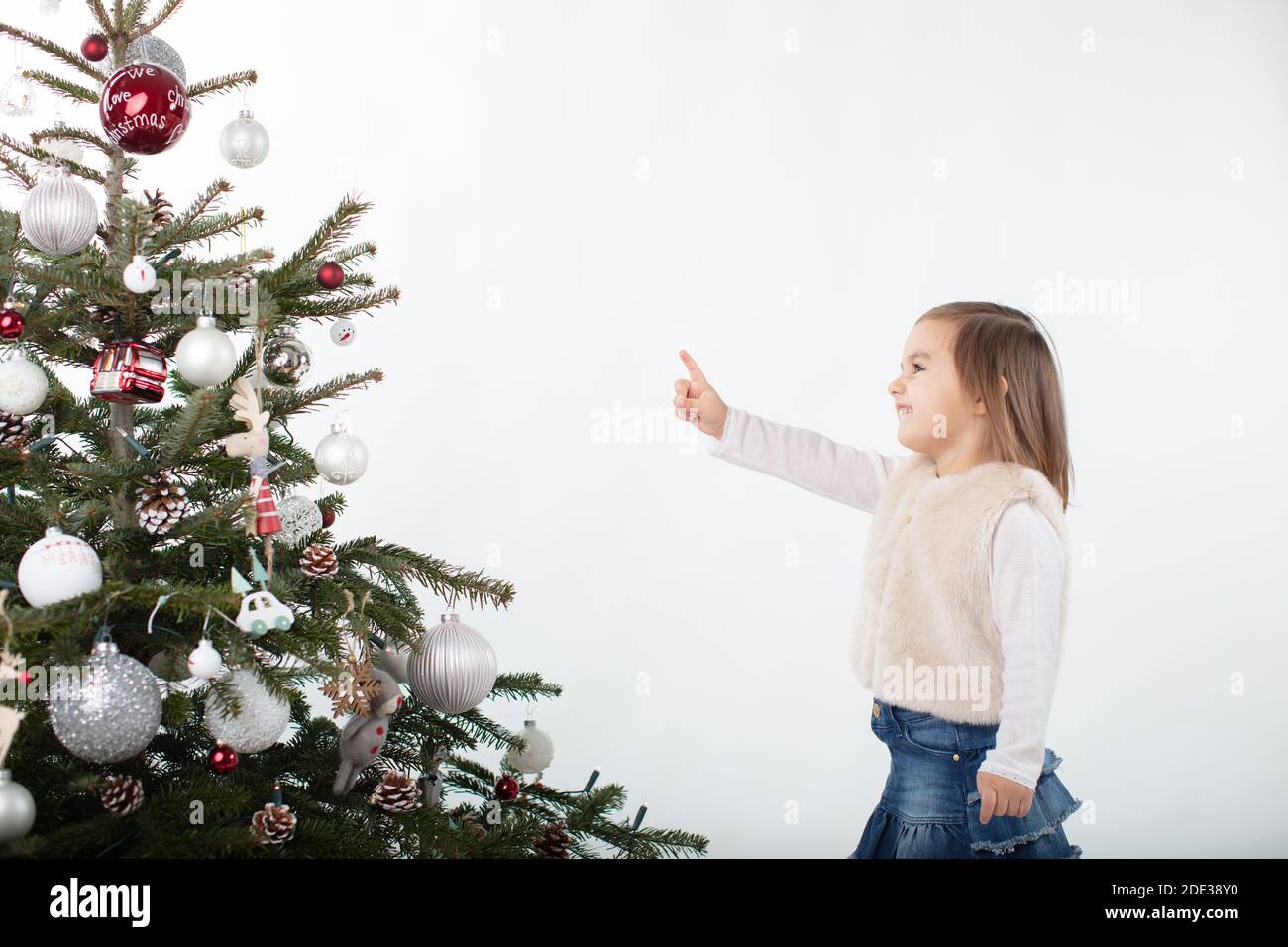 Cheeky toddler girl pointing towards the tip of the Christmas tree Stock Photo