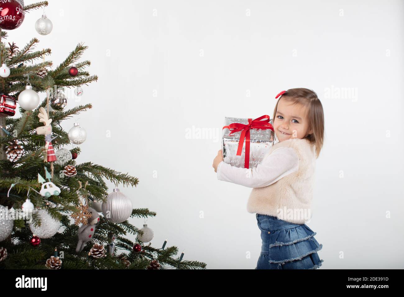 Smiling toddler girl holding tight her Christmas gift box. Merry Xmas! Stock Photo