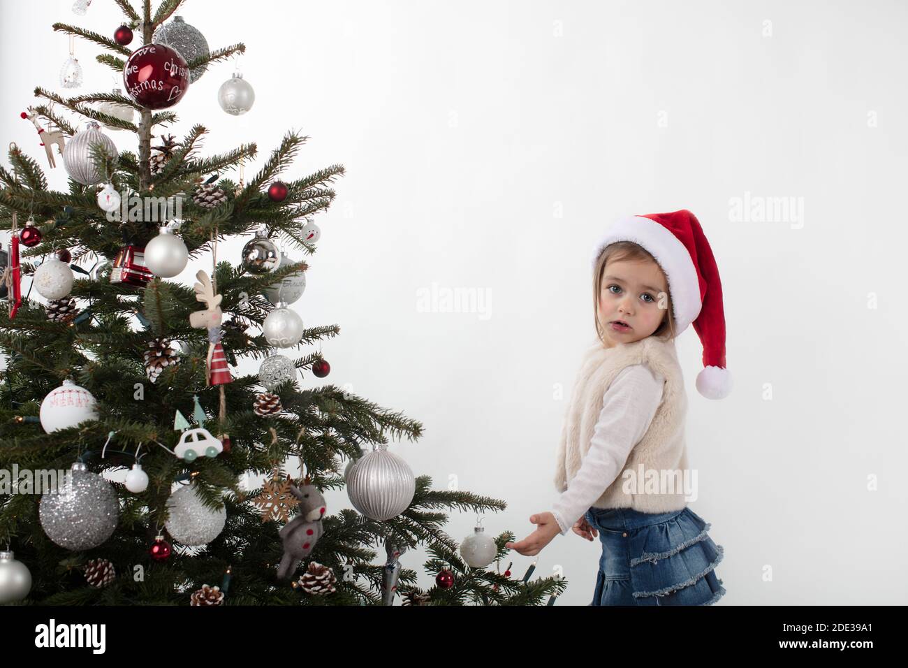 Sweet little girl next to Xmas tree on white background Stock Photo