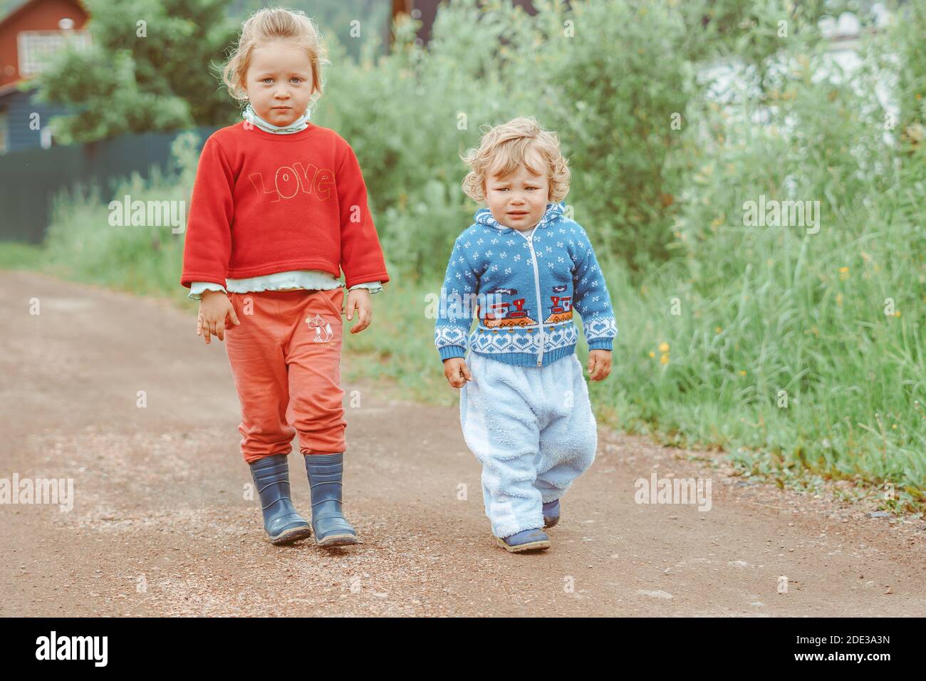 sister and brother walking down the street in a small village among the ...