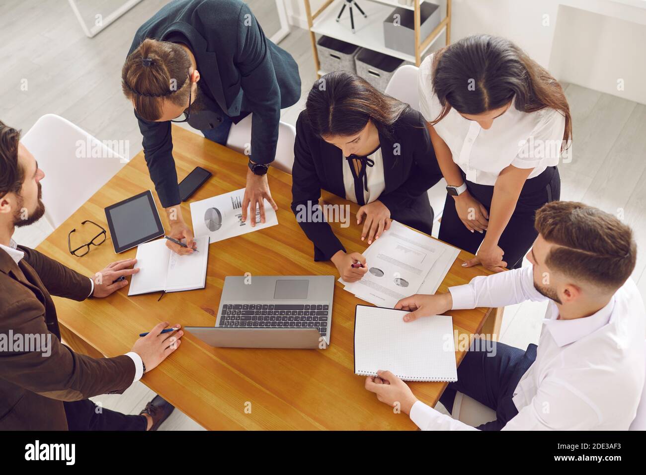 Sales team gather around office desk, analyze financial data and do