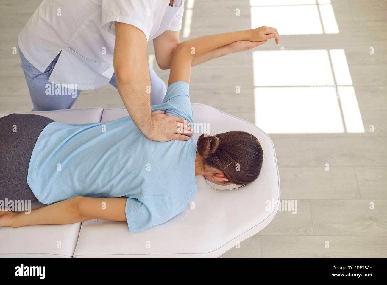 Hands of osteopath masseur doctor fixing lying woman patients back and shoulder Stock Photo