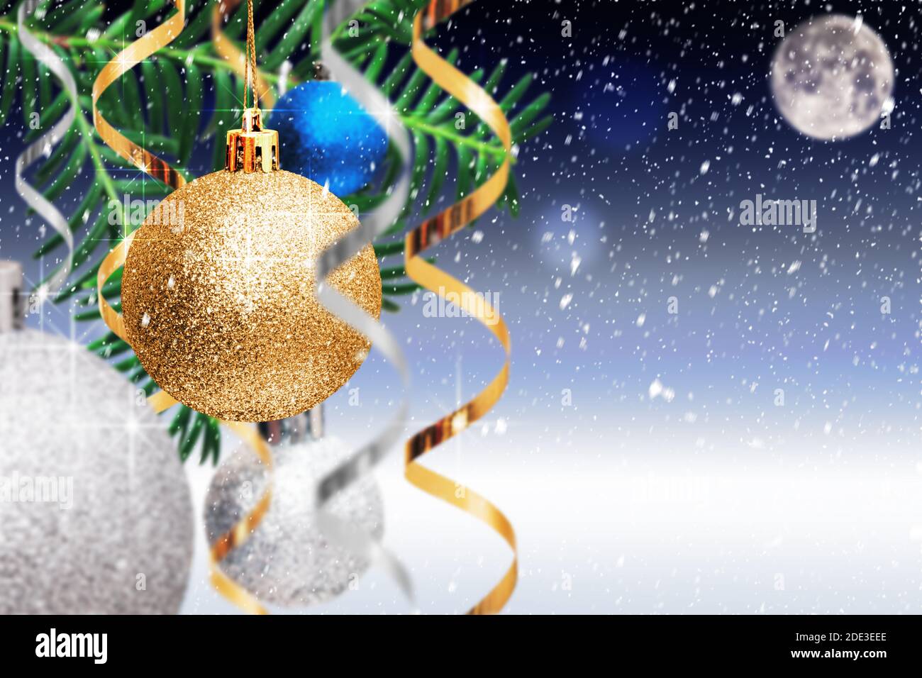 Christmas decoration. Golden and silver balls, streamers hanging on spruce branch on blue snowy background. Christmas card with copy space Stock Photo