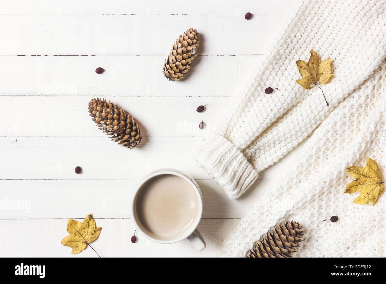 Autumn or winter composition. Cup of coffee, women fashion sweater, pine cones and fall leaves on white wooden background. Flat lay, top view, copy sp Stock Photo