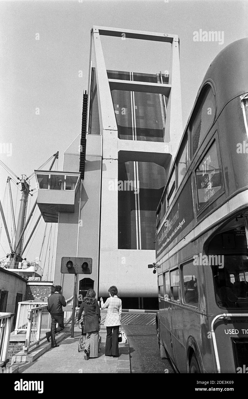 UK, London, Docklands, Isle of Dogs. South West India dock entrance, Preston's Rd / Manchester Road E14. London double-decker red bus (type RT) stopped at the raised Blue Bridge, heading north, as a ship passes through the channel that runs between the River Thames & the West India south dock. 1970's fashionable wide-bottomed trousers for the women and pencil trousers for the young man. Stock Photo