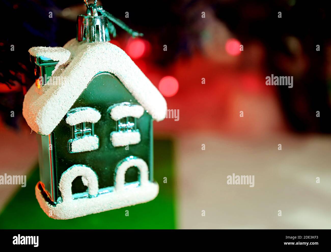 Closeup Snow-covered Green Little House Ornament with Red Christmas Decorating Light Bokeh  in background Stock Photo