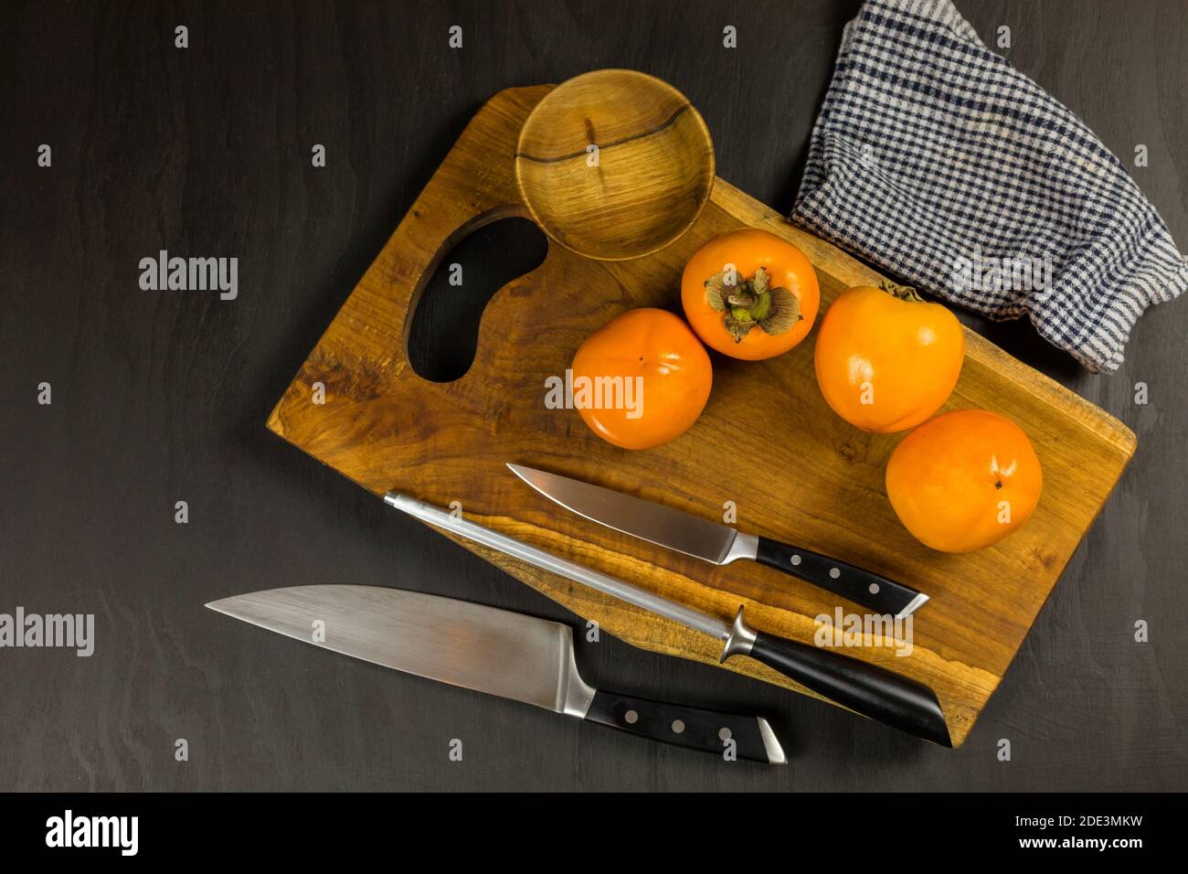 Ripe fresh persimmons on rustic background. Kaki fruit on wooden kitchen table. Slicing fruit on a kitchen board. Stock Photo