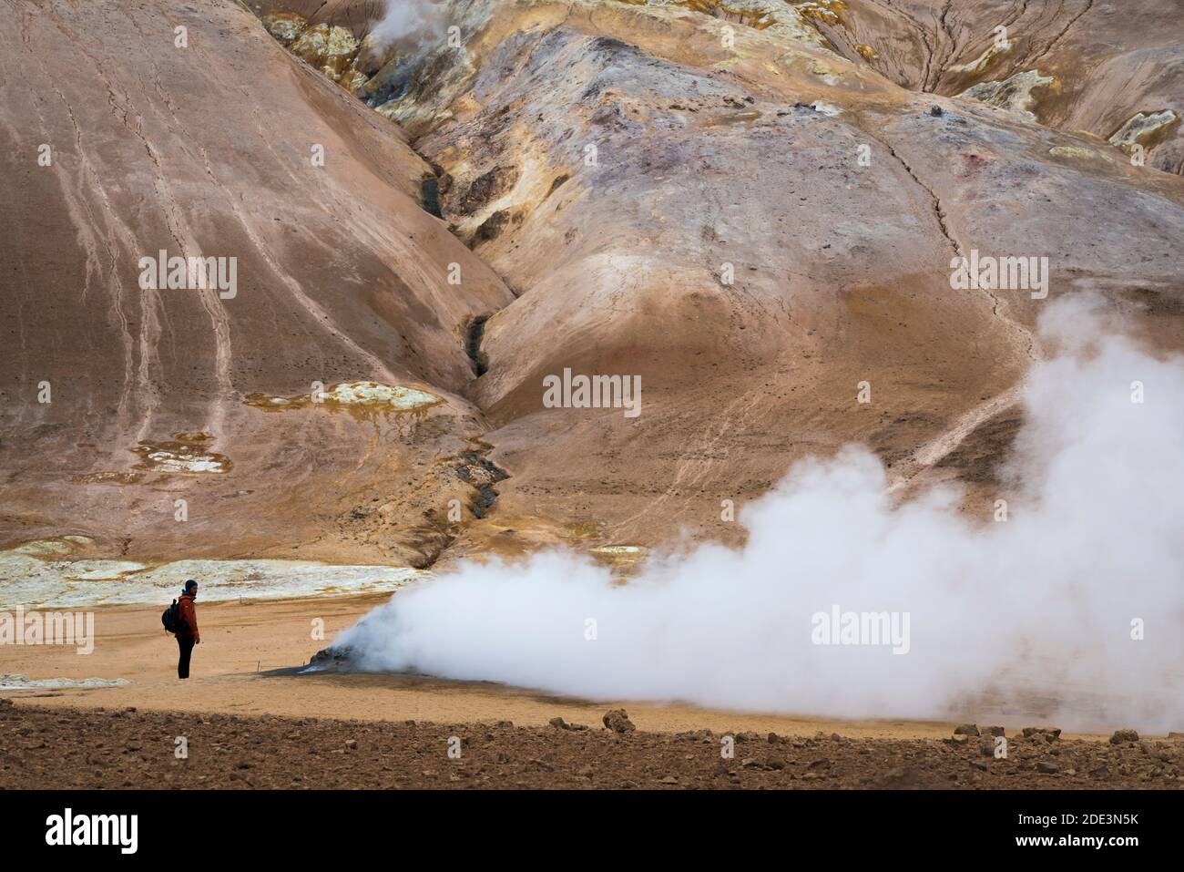 Young man standing by smoking fumarola in geothermal area, Namafjall Hverir, Northern Iceland Stock Photo