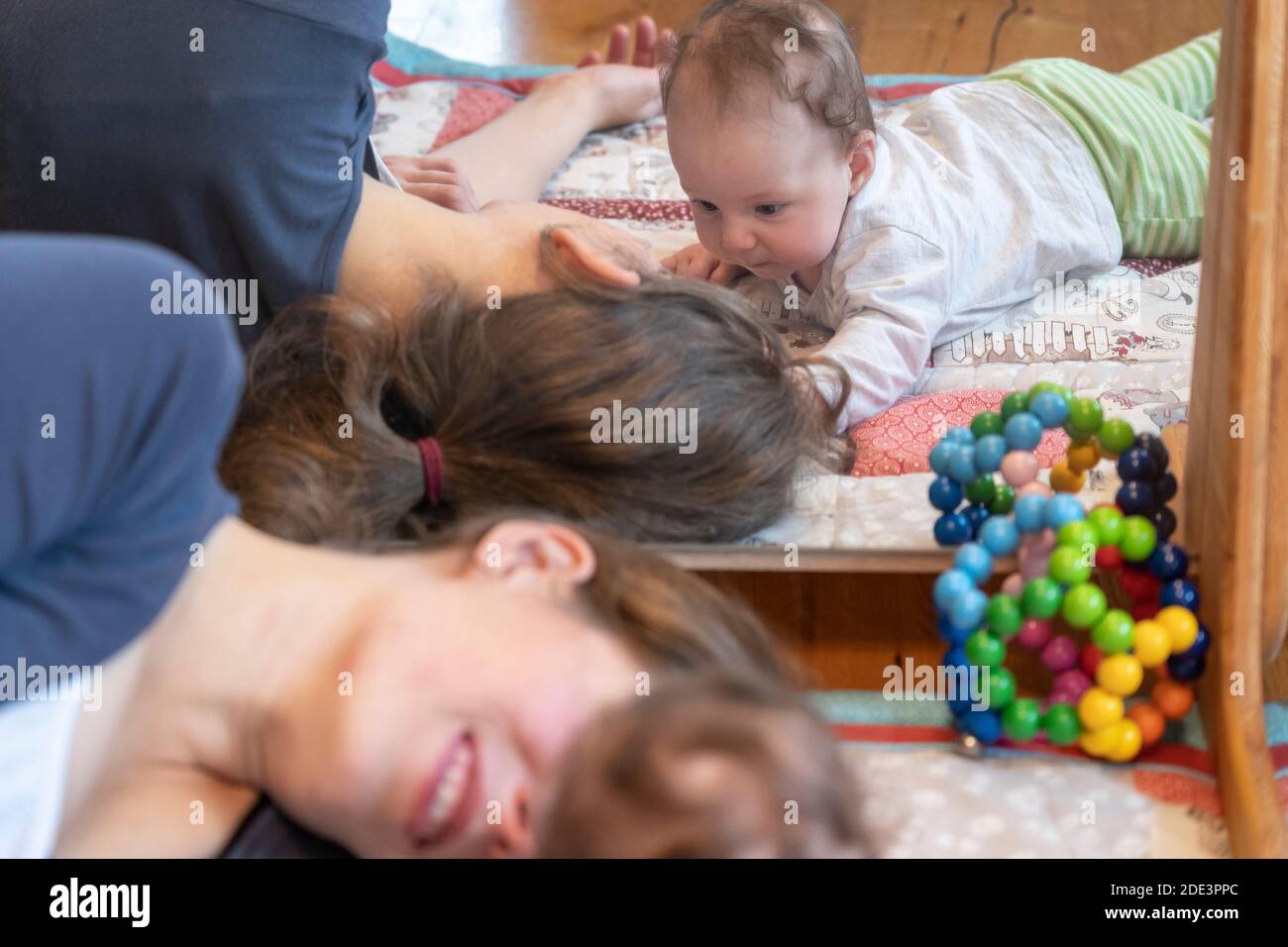 A mother interacting and playing with her 4 month old baby daughter, with both lying down on a play mat with a mirror behind, UK Stock Photo
