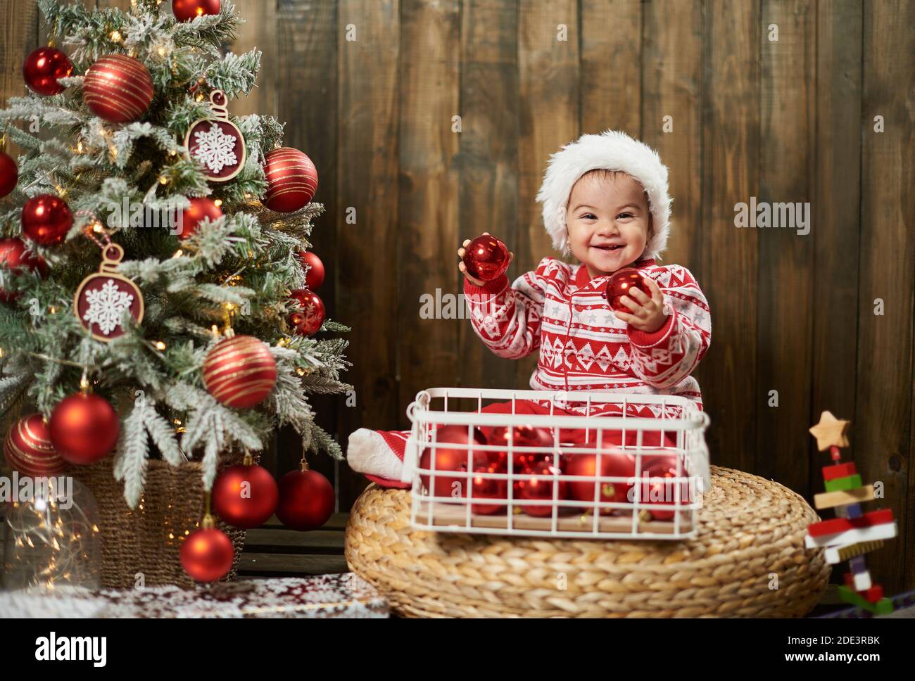 Smiling baby girl with christmas balls next to christmas tree Stock Photo