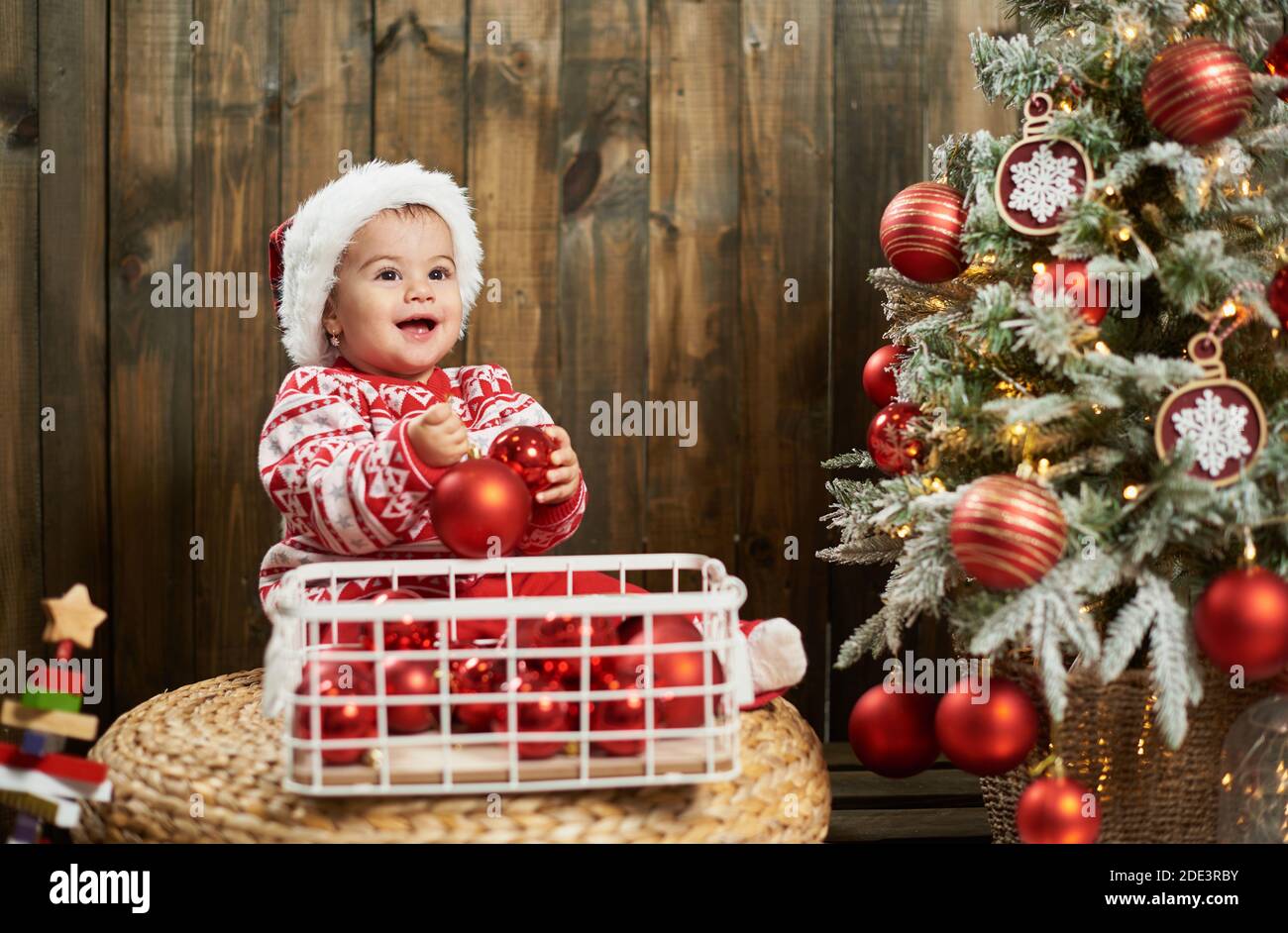 Smiling baby girl with christmas balls next to christmas tree Stock Photo