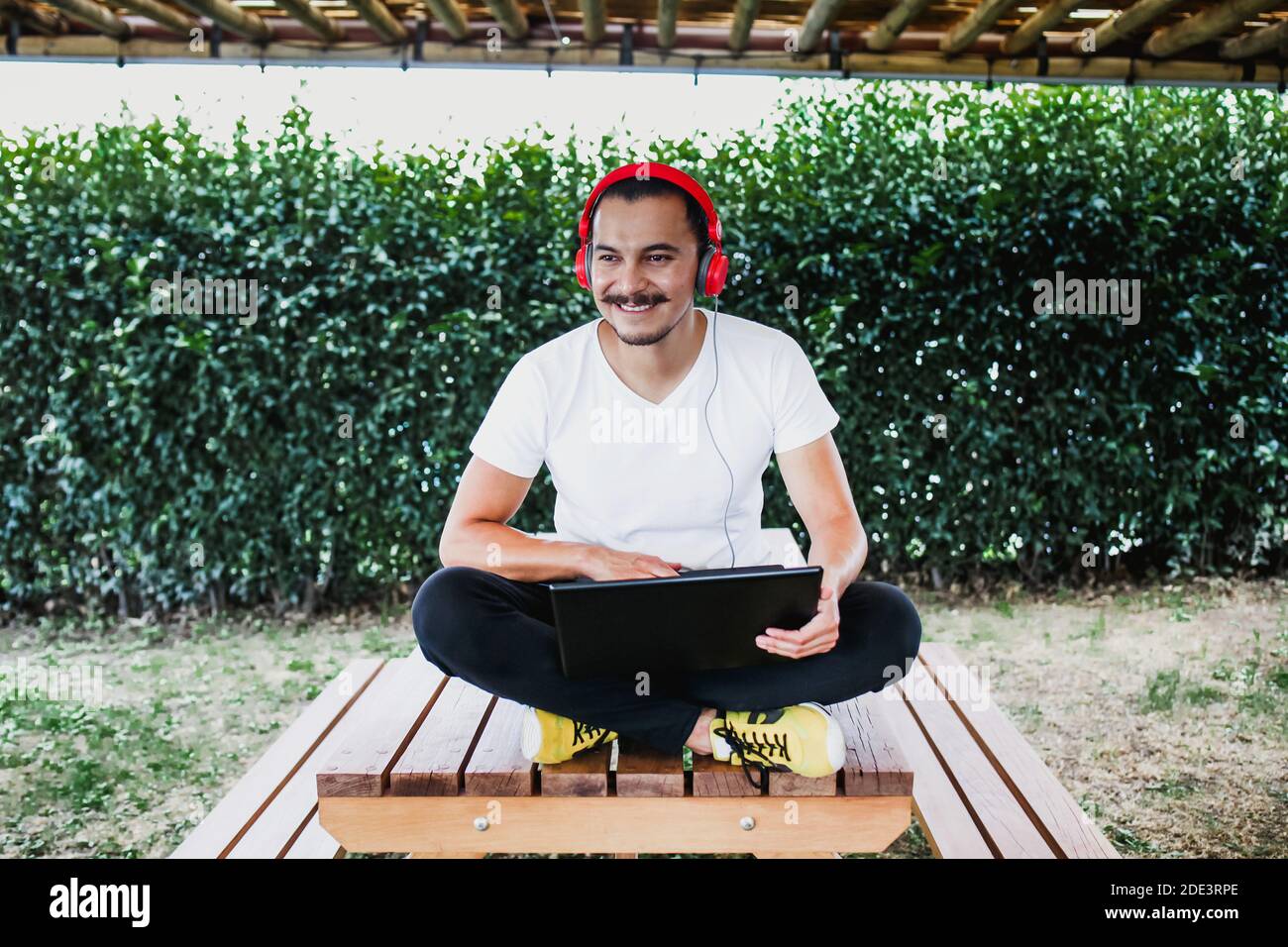latin man with laptop and headphones at home terrace outdoor in Mexico Stock Photo