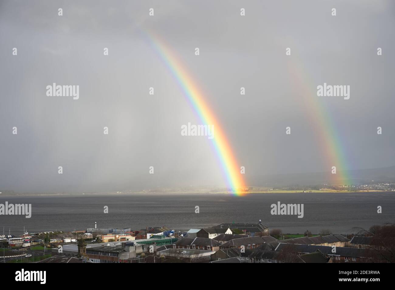 Bright rainbow high in sky over the sea during dark storm Stock Photo