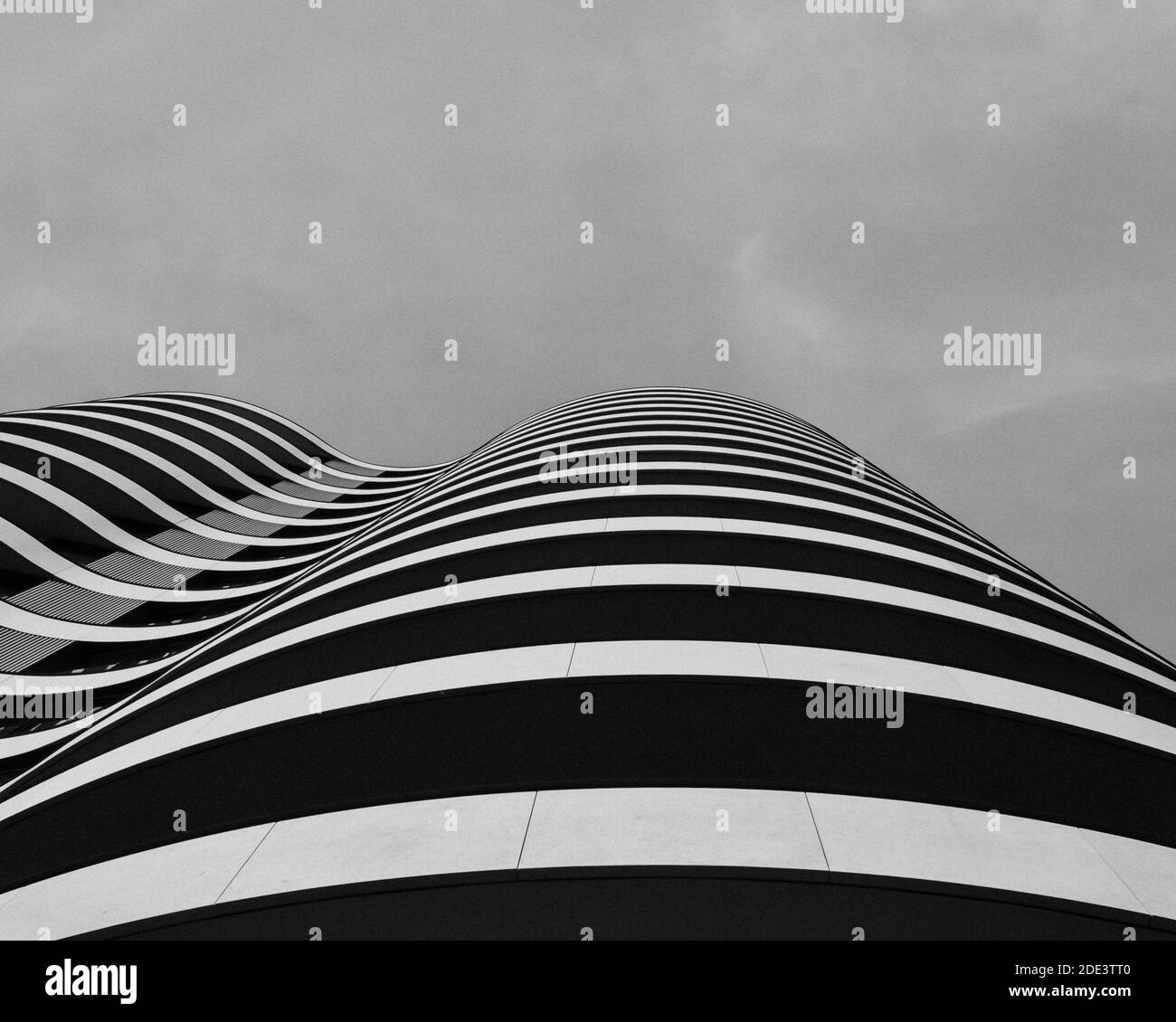 A grayscale shot of a modern curved building under a cloudy sky Stock ...