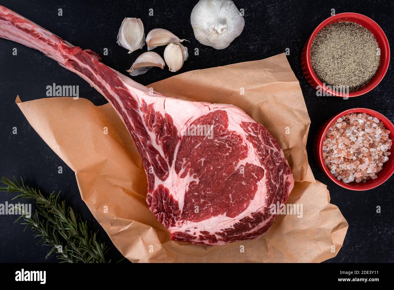 Freshly cut tomahawk ribeye steak with butcher's paper ready to be seasoned with salt and pepper, garlic and rosemary on a countertop Stock Photo