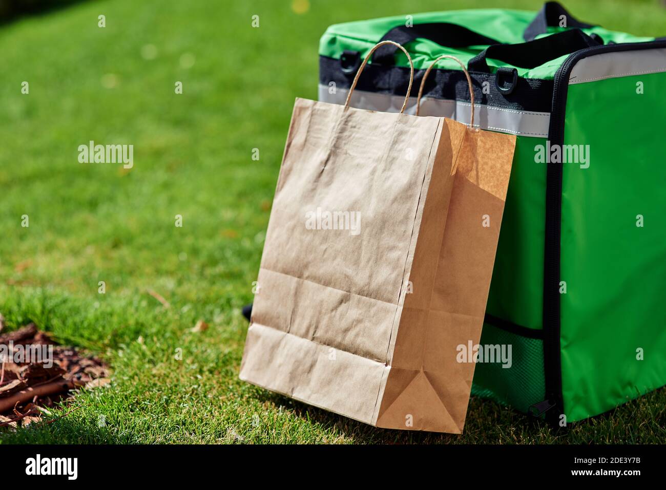 Fast delivery. Green thermal backpack and paper bag standing on the green  grass outdoors, close up shot. Food delivery services and shopping online  concept Stock Photo - Alamy