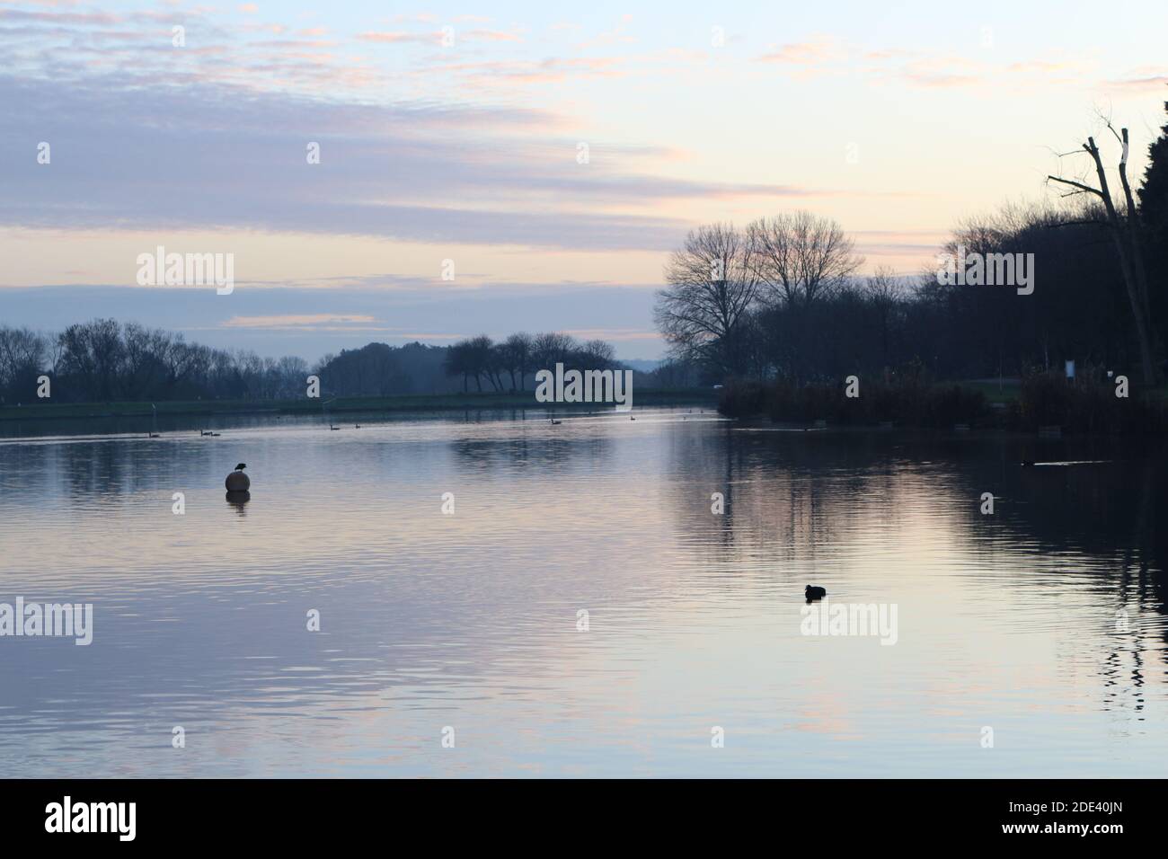 View at sunset with scenic sky, clouds at the horizon reflected on a lake in a cold autumn day, cold and worm colour mixing together at dusk Stock Photo