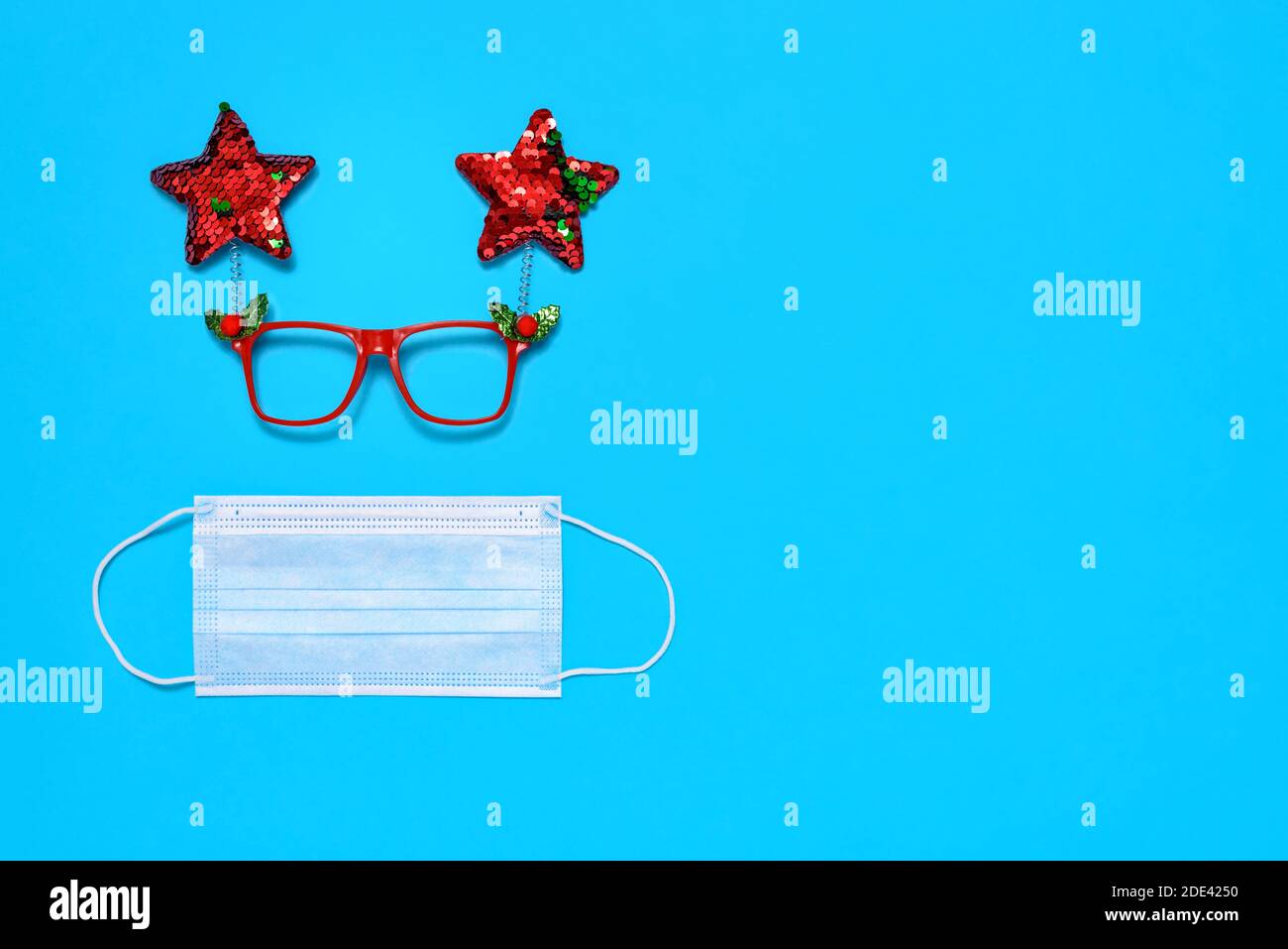 Medical mask and decorative Christmas glasses on blue background. The concept of celebrating the New Year and Christmas during the COVID-19 epidemic. Stock Photo