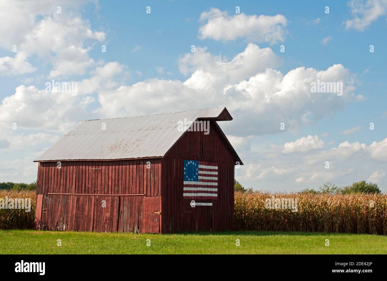 A wooden barn with a painting of the 13-star Betsy Ross flag (an early American flag design) stands near cornfields along old Route 66 in Nilwood, IL. Stock Photo