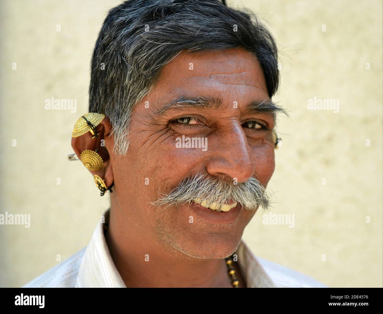 Middle-aged positive cheerful Indian Gujarati man with grey moustache and elaborate gold ear jewelry (ear lobe and ear helix) smiles for the camera. Stock Photo