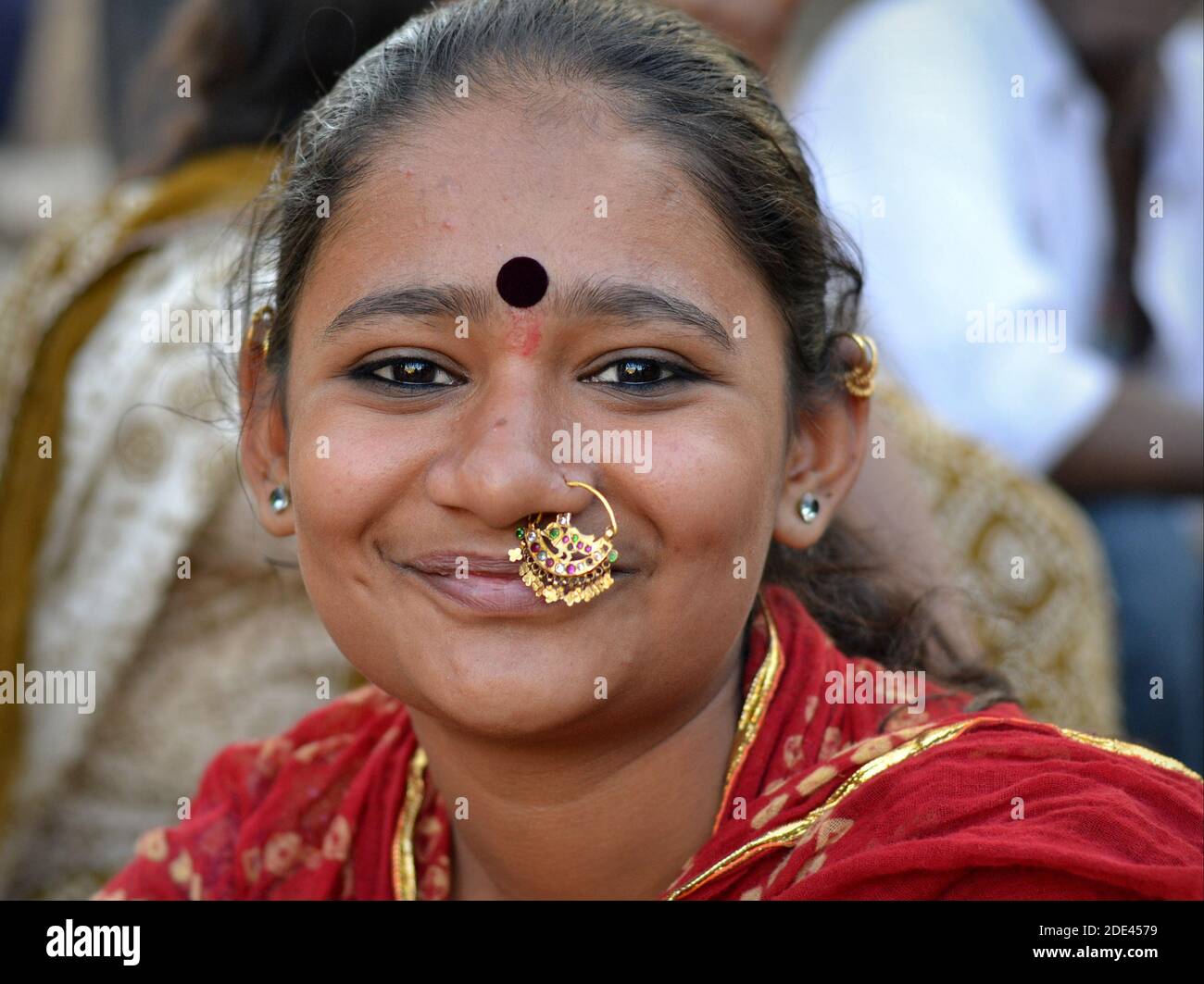 Young beautiful positive Indian Gujarati woman with large elaborate gold nose jewelry (nose ring) and large bindi on forehead smiles at camera. Stock Photo