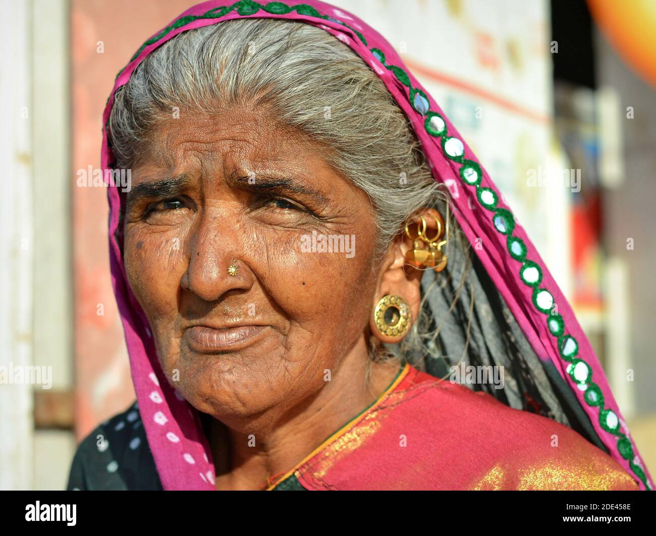 Old Indian Gujarati woman with elaborate ear jewelry (ear lobe plugs, ear helix piercings) and traditional head scarf (dupatta) poses for the camera. Stock Photo