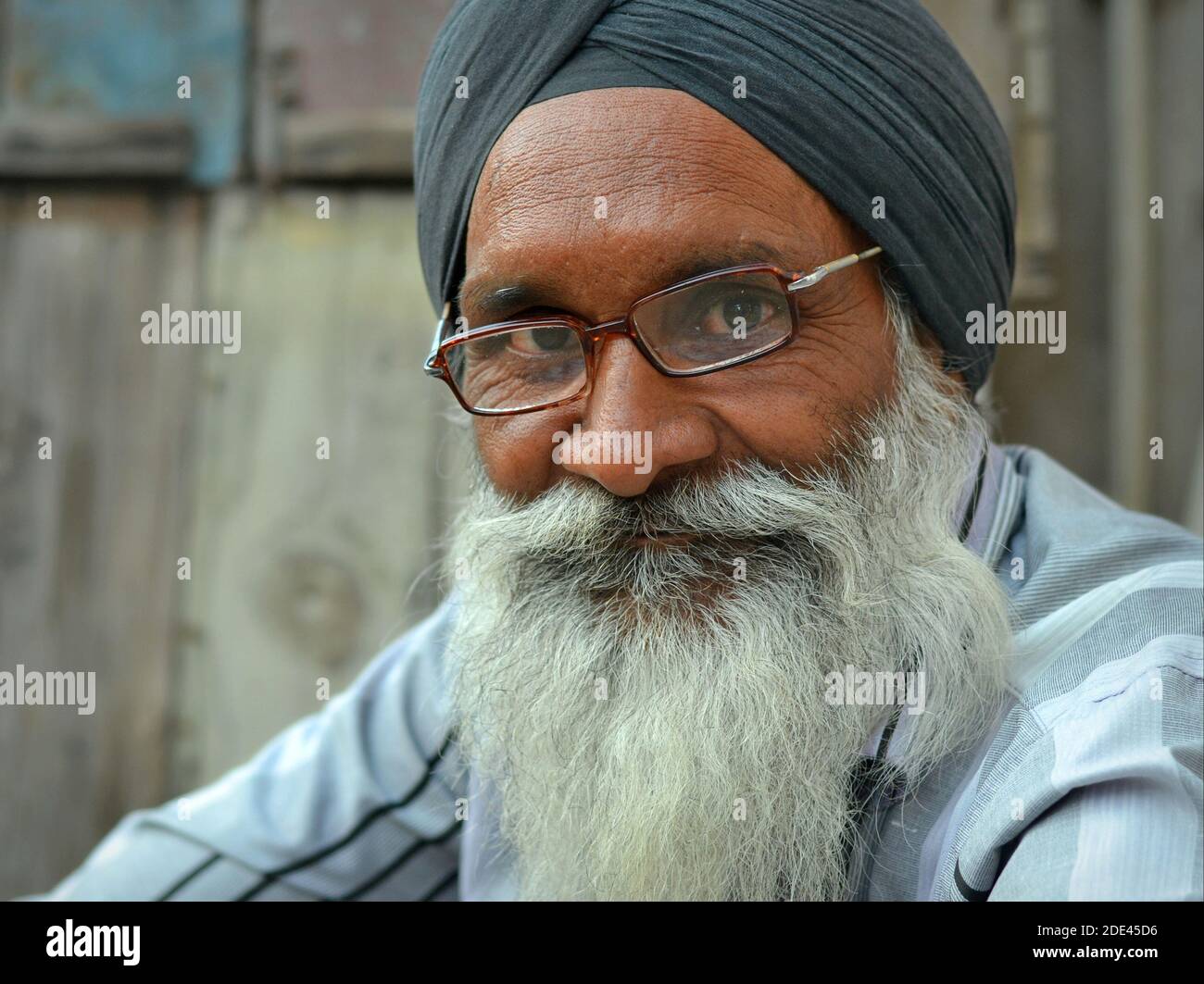 Friendly elderly Indian Sikh man with traditional black dastar turban, long white beard and rectangular eyeglasses poses for the camera. Stock Photo