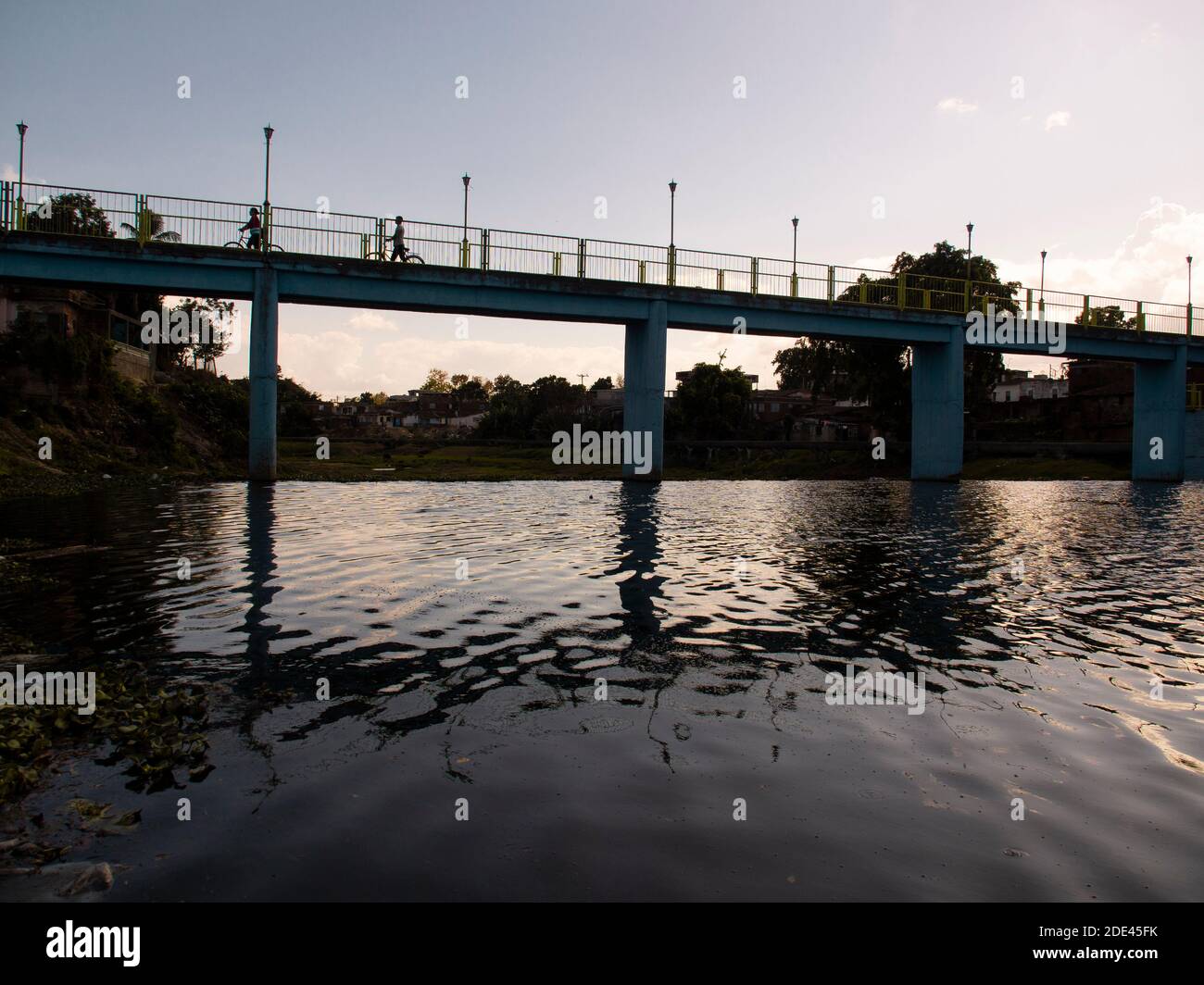 People crossing a river by a bridge, the bridge is reflected in the river, sunset Stock Photo