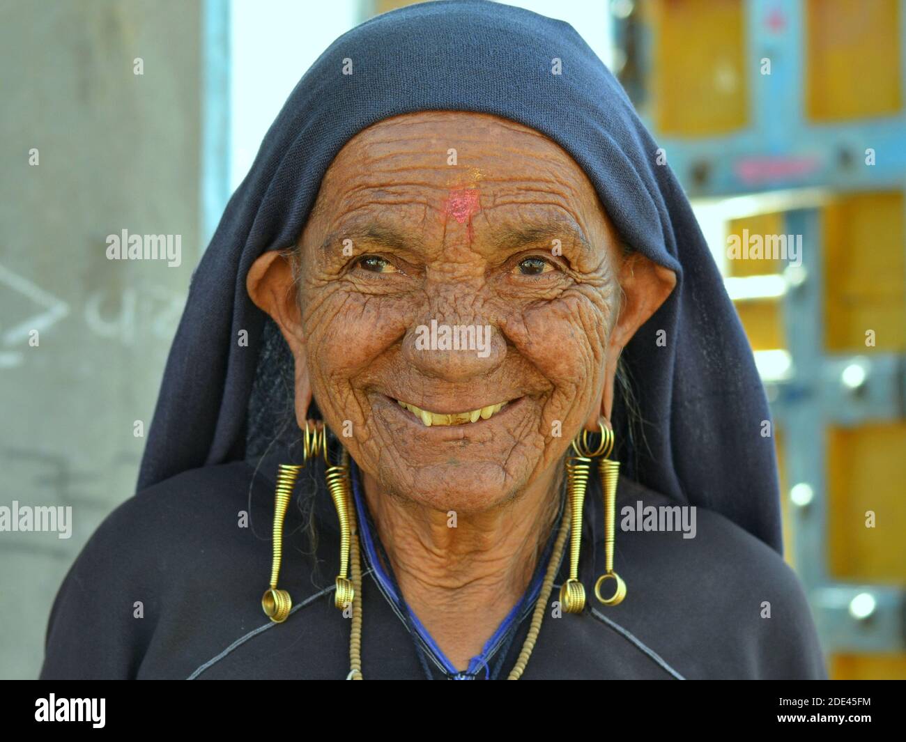 Old Indian Gujarati Rabari woman with face wrinkles and tribal snake earrings (nagali) in her elongated ear lobes smiles at the camera. Stock Photo