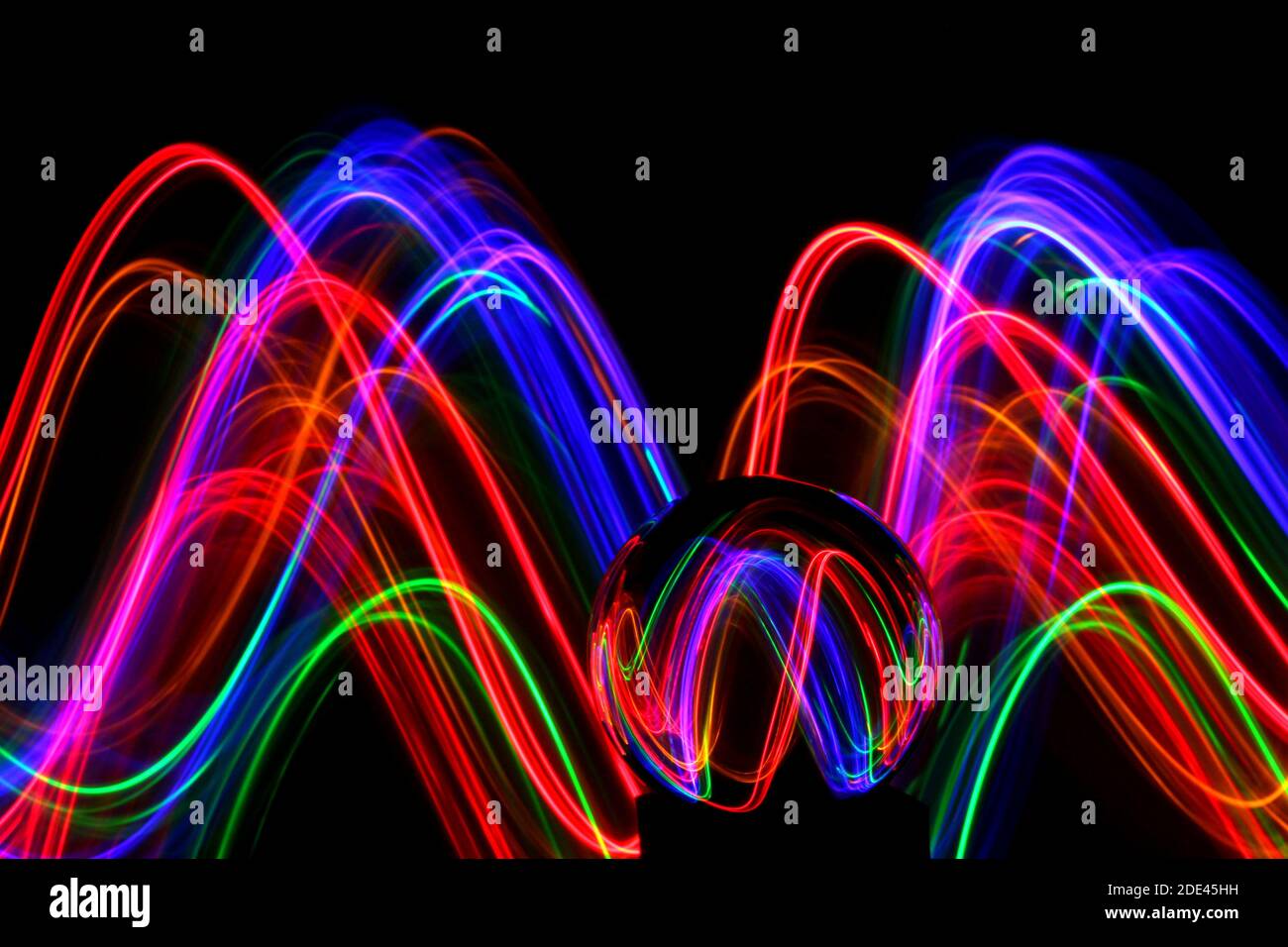 Long exposure photograph of neon multi colour in an abstract swirl pattern with reflective glass ball. Light painting photography. Stock Photo