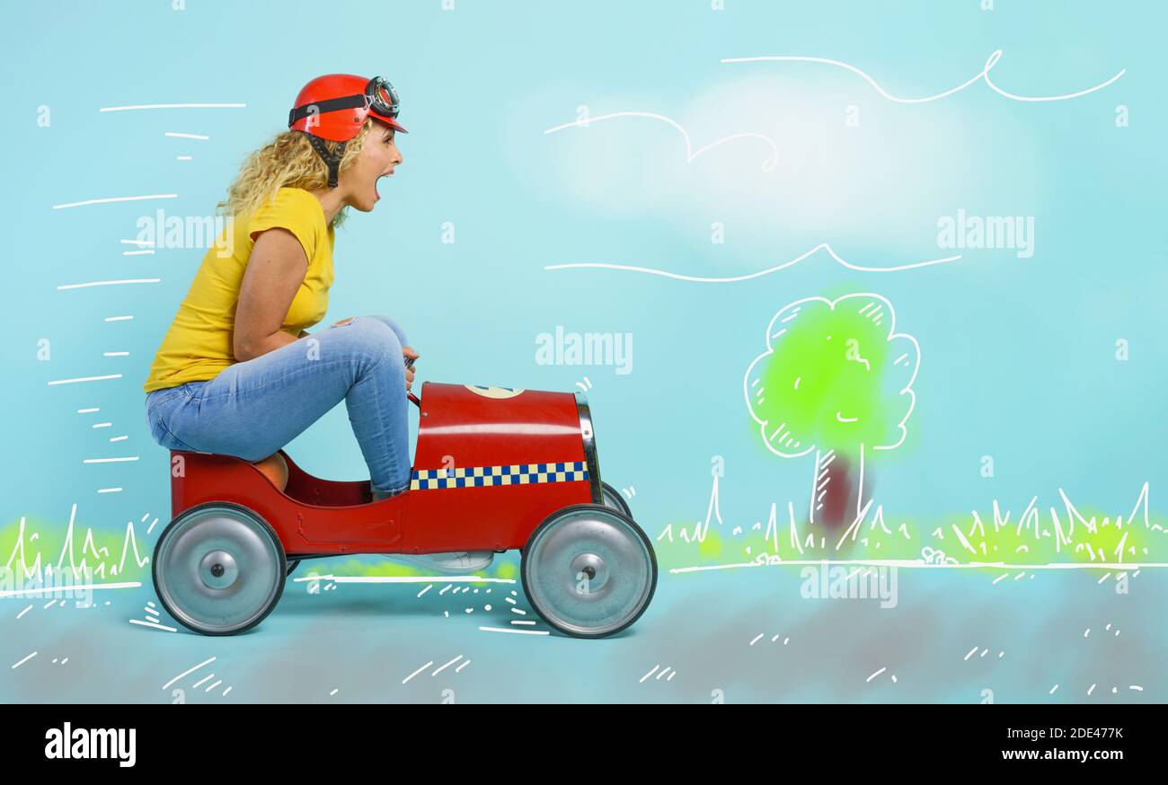 Woman with red helmet drives a fast toy car. cyan background. Stock Photo
