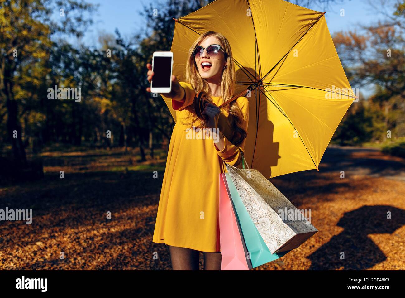 Stylish happy girl with yellow umbrella on the street, holding shopping ...
