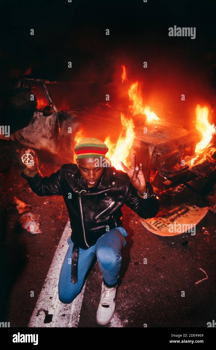 Anti-Gulf War demonstration Jan. 17th 1991. San Francisco, CA, USA.  A young black man wearing a Pan-African colored hat and holding a peace sign kneels in front of a burning police car at the entrance to the San Francisco Bay Bridge.  The young man pictured was attempting to stop the violence during the protest.  NOTE: This is a file photo taken in 1991. Stock Photo