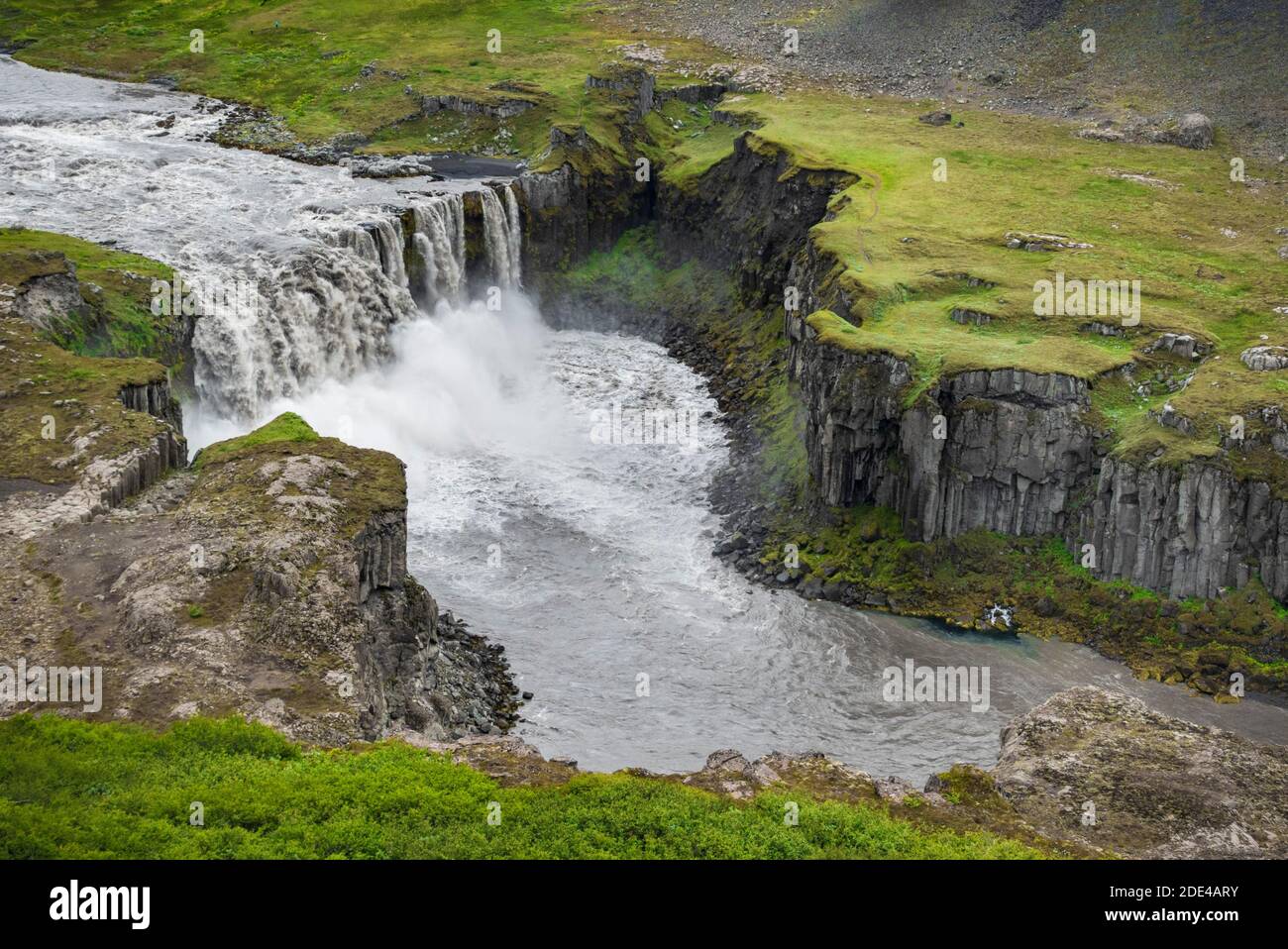 Waterfall falls from green volcanic plain over basalt columns into a canyon, Hafragilsfoss, Joekulsargljufur National Park, Norourping Stock Photo
