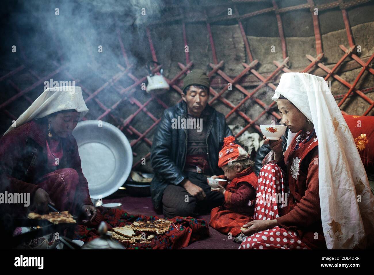 A man, two woman, a child at mealtime, nomadic Kyrgyz, yurt, a woman drinking milk tea from a bowl, Bozai Gumbaz, Wakhan Corridor, Badakhshan Stock Photo