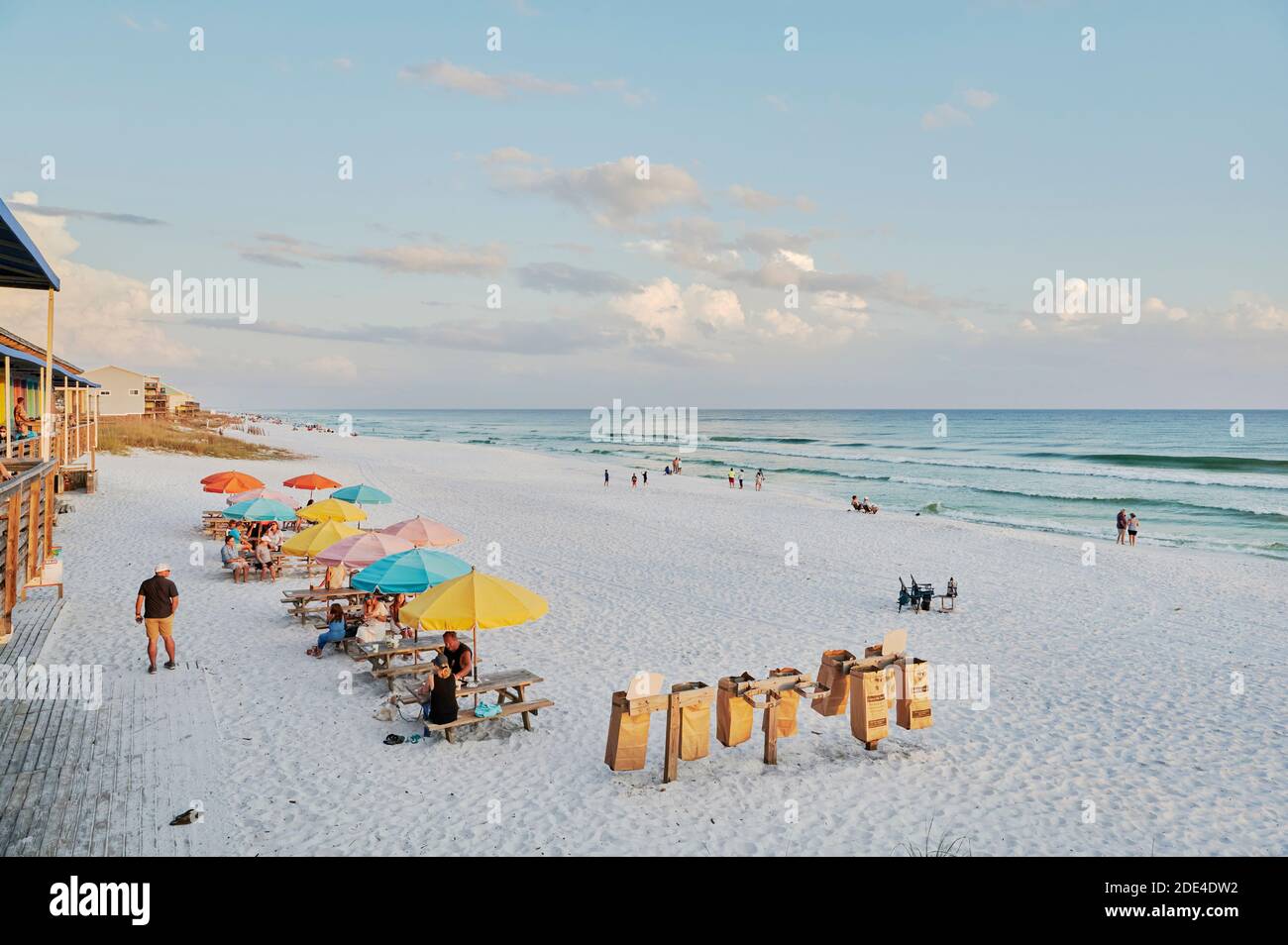 People relaxing on the white sand beach at sunset next to a beach bar