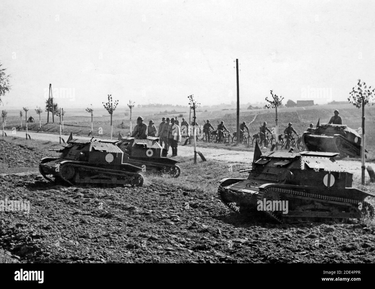 TK-3 tankettes when crossing the road. In the background, a team of cyclists leading bikes is visible. Poland,  September 1938 Stock Photo