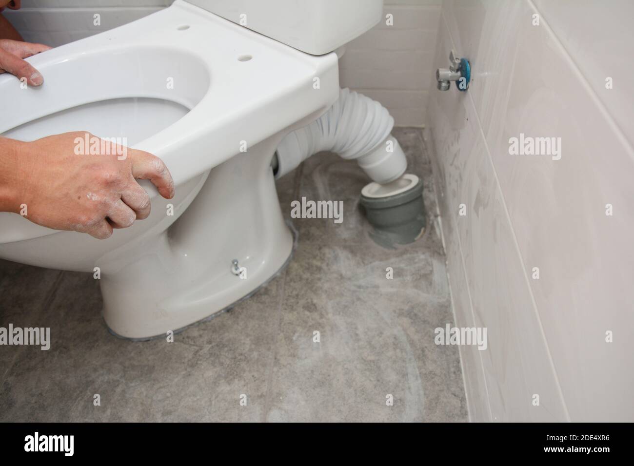 A handyman is installing a flush toilet. Repairing, dismantling toilet bowl in the bathroom. Stock Photo